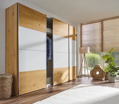 Moderner Schiebetürenschrank in Eiche und Weiß mit dekorativen Holzlamellen, integriert in helles Schlafzimmer mit Holzfußboden und großen Fenstern, ideal für stilvolle Stauraumlösungen.